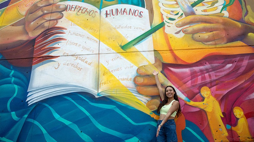 A woman signals with her arms towards a mural about human rights.