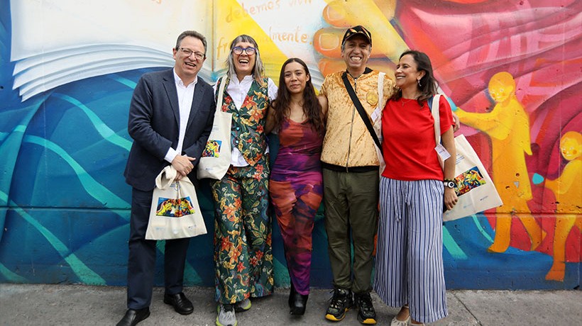 A group of people stand in front of a colourful wall. 