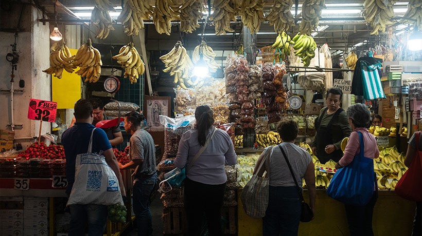 Six people standing in a fruit stand in a market.