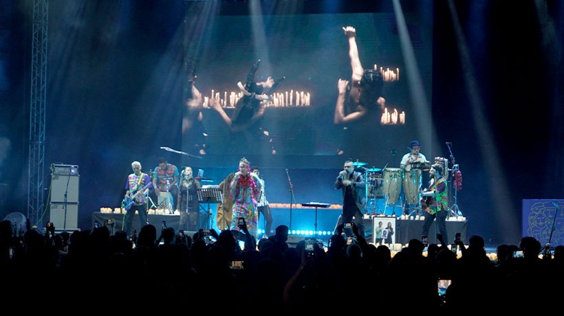 People in a scenario singing and playing instruments with a screen behind showing dancers and candles.