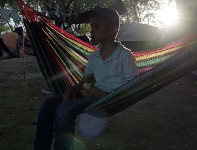A boy sits in a hammock. Tents are in the background.