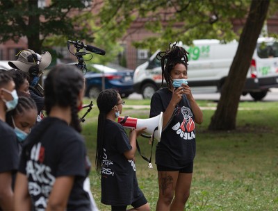 Instantánea de Bianca Jones de pie junto a jóvenes organizadores en Douglass Park a la vez que se dirigen al público que ha venido a mostrar su apoyo al cambio de nombre del parque con su campaña Relaunch Rally, el 18 de julio de 2020. © Kaleb Autman