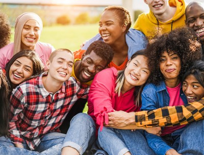 Un grupo de personas de diversos orígenes étnicos sentadas juntas, abrazándose y riendo. Crédito: Getty Images/DisobeyArt. 