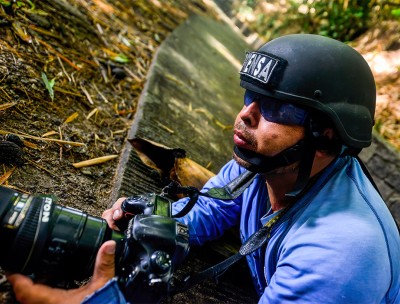 Journalist wearing a press helmet angles his camera. © Carlos Herrera