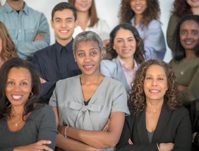 A group of women with their arms crossed look at the camera while smiling.