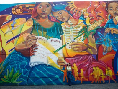 A woman stands in front of a wall featuring a colourful mural. 