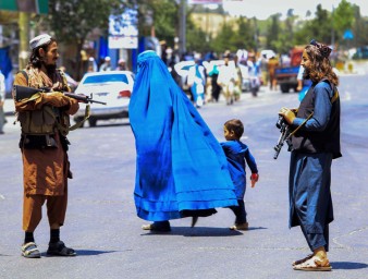 Afghan woman and child walking past Taliban soldiers © Credit – EPA-EFE