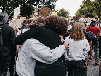 Two women in a crowd embrace as they demonstrate for racial justice, Seattle, USA, 10 June 2020. © Duncan Shaffer/UNSPLASH