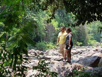 A man and a woman stand on a stone near a river