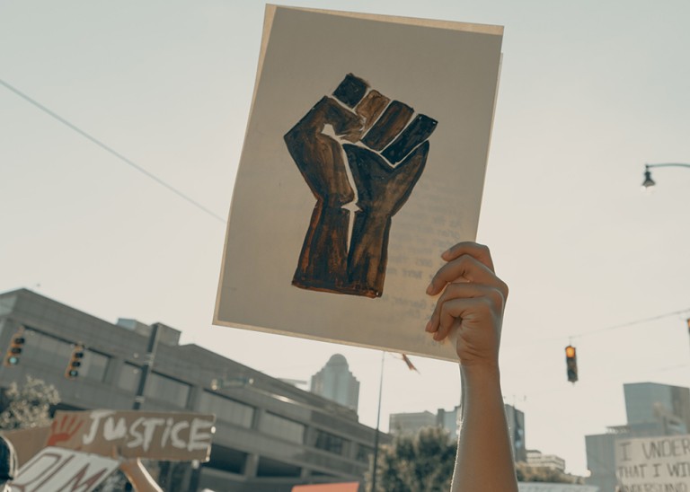 A woman in a crowd holds a demonstration sign depicting a balled fist, Charlotte, NC, USA, 3 June 2020 © Clay banks/UNSPLASH